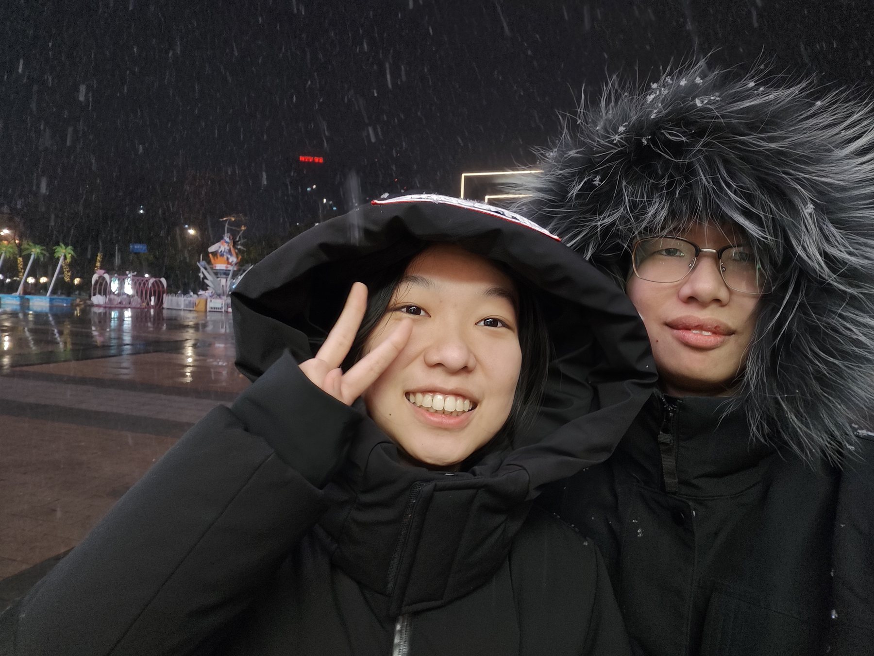 雪夜里，两个人穿着厚外套对镜头合影